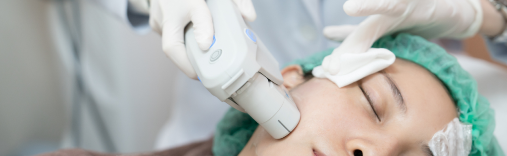 A client undergoing an aesthetic treatment with a specialised machine. The machine is positioned near the client's face, emitting gentle, precise energy or light onto the skin. The client appears relaxed and comfortable during the procedure.