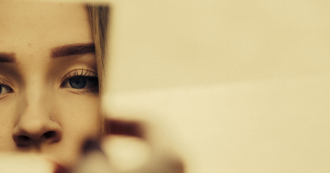 Close-up of a woman gazing at herself in the mirror, reflecting feelings of self-consciousness and body image concerns.