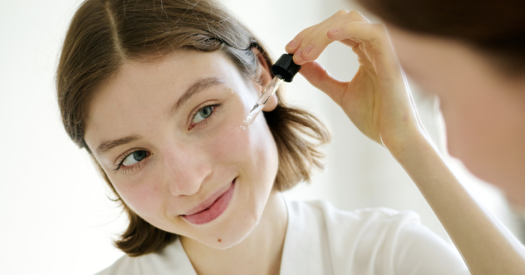 Woman gently using a dropper to apply retinol serum on her cheek for smoother, clearer skin.