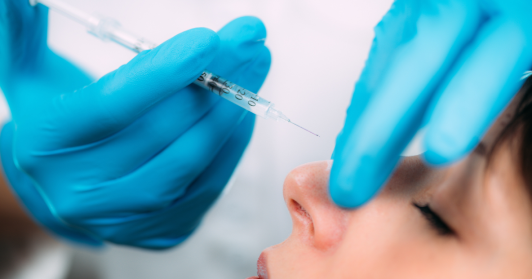 Female patient undergoing non-surgical rhinoplasty with a practitioner carefully injecting dermal fillers into the nose.