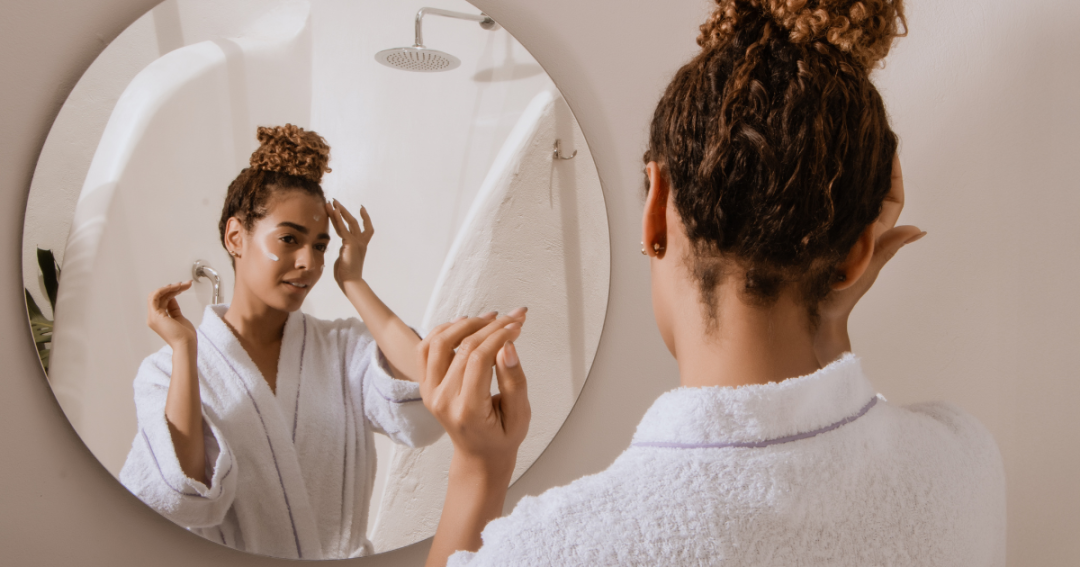 Understanding the Best Skincare Routine 1 A woman applying skincare cream to her face in front of a mirror.