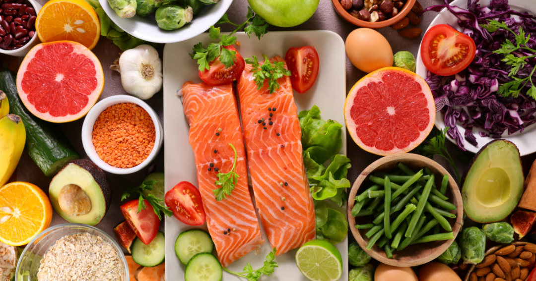 Glow From Within: How Nutrition and Lifestyle Transform Your Skin 1 Array of healthy foods including leafy greens, colorful fruits, nuts, and whole grains arranged on a table.