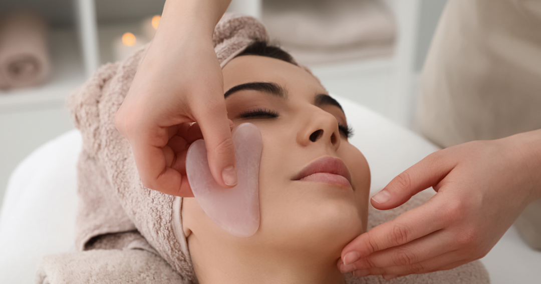 A client receiving a Gua Sha facial massage with a smooth stone tool to improve circulation and skin appearance."
