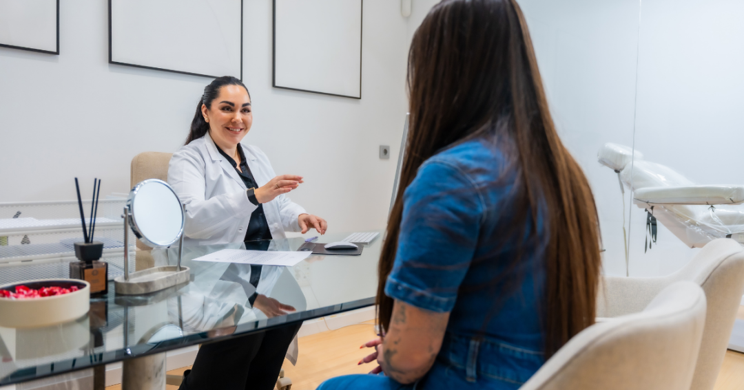 A patient sitting across from an aesthetic practitioner during a facial consultation, discussing treatment options for skin and facial concerns.