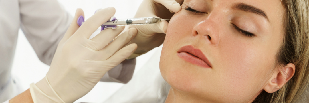 Practitioner injecting dermal filler into a patient's lips during treatment.