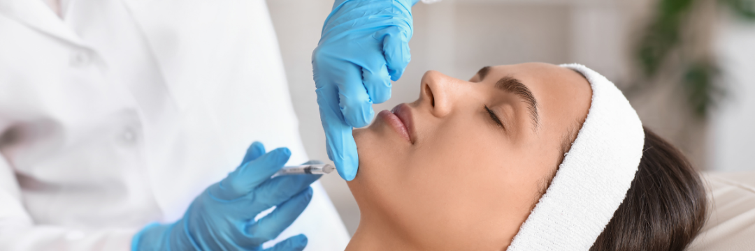 Gloved practitioner administering dermal filler to a patient's chin with a syringe.